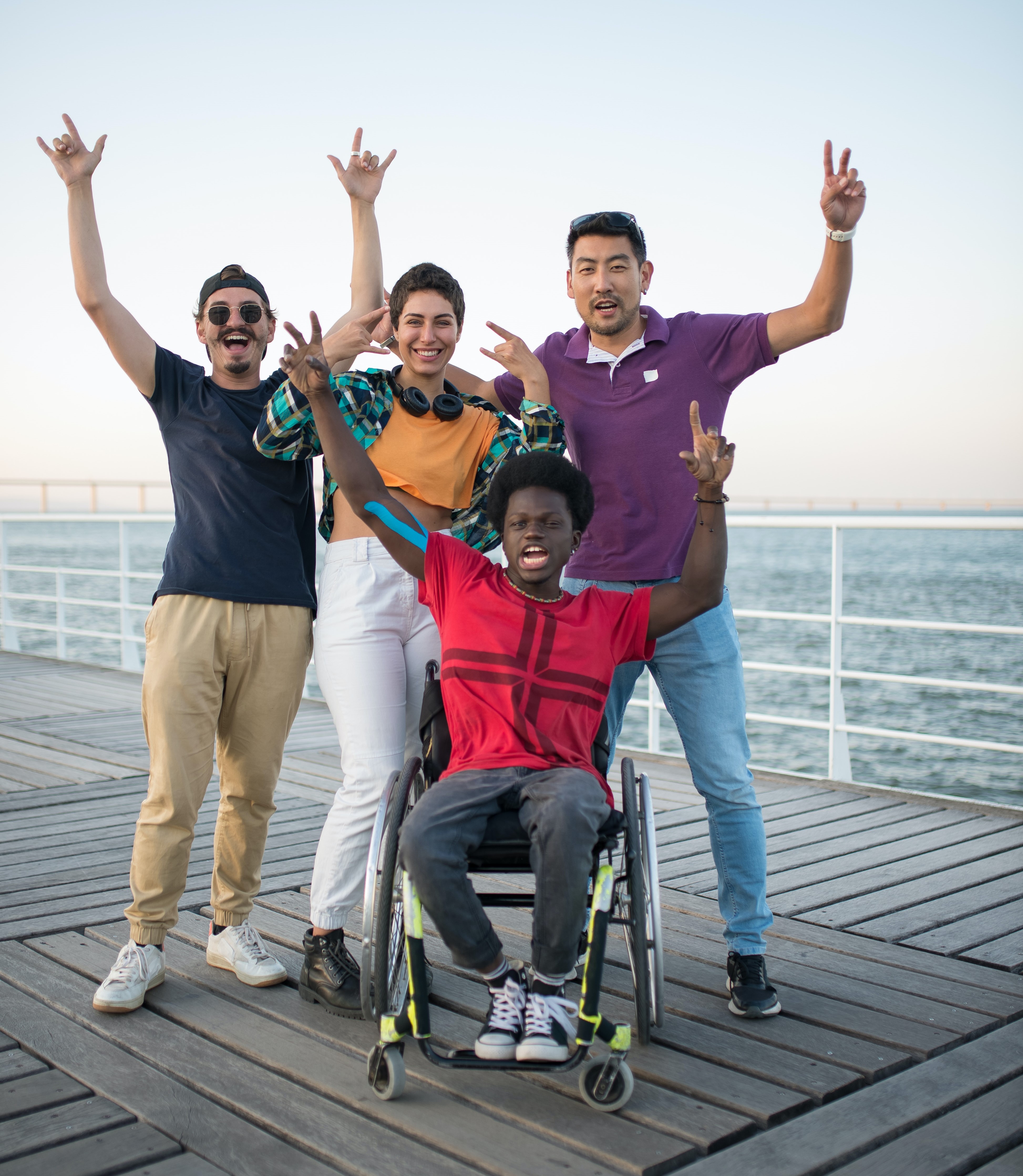 three young racially and gender diverse adults stand behind a black young adult on a beach boardwalk with their arms raised.